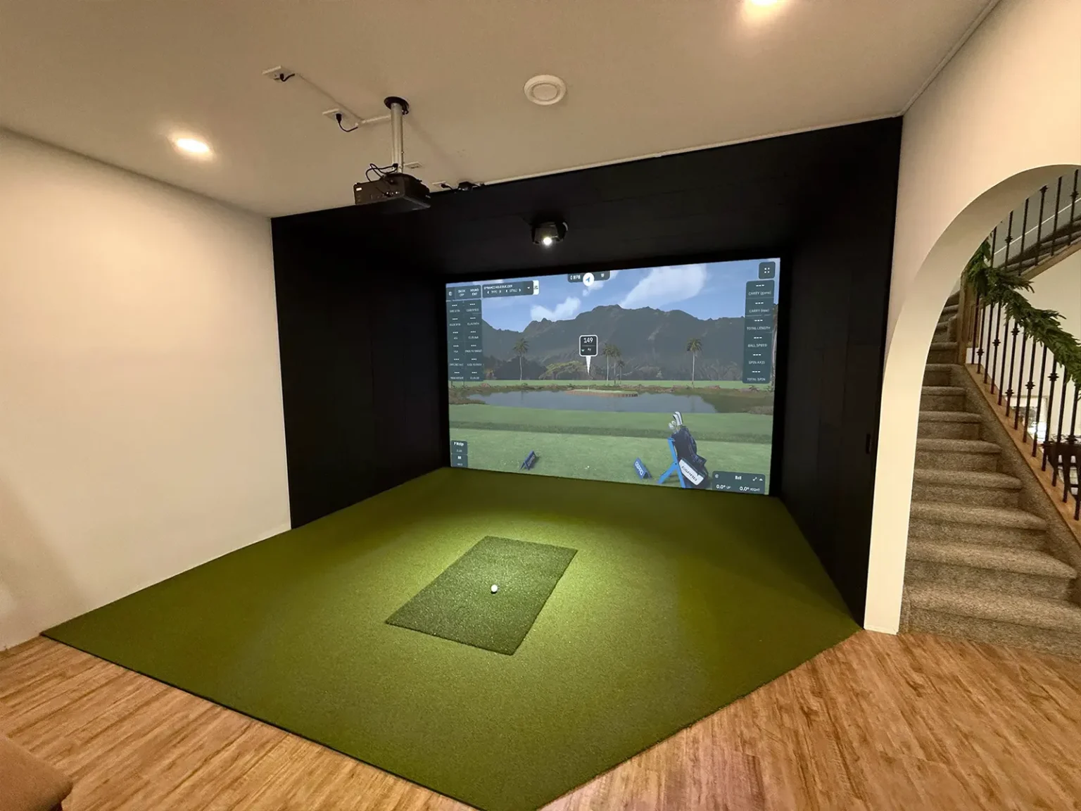 Basement golf simulator room by Alberta Golf Sim with black enclosure, impact screen, turf and ceiling-mounted projector and launch monitor