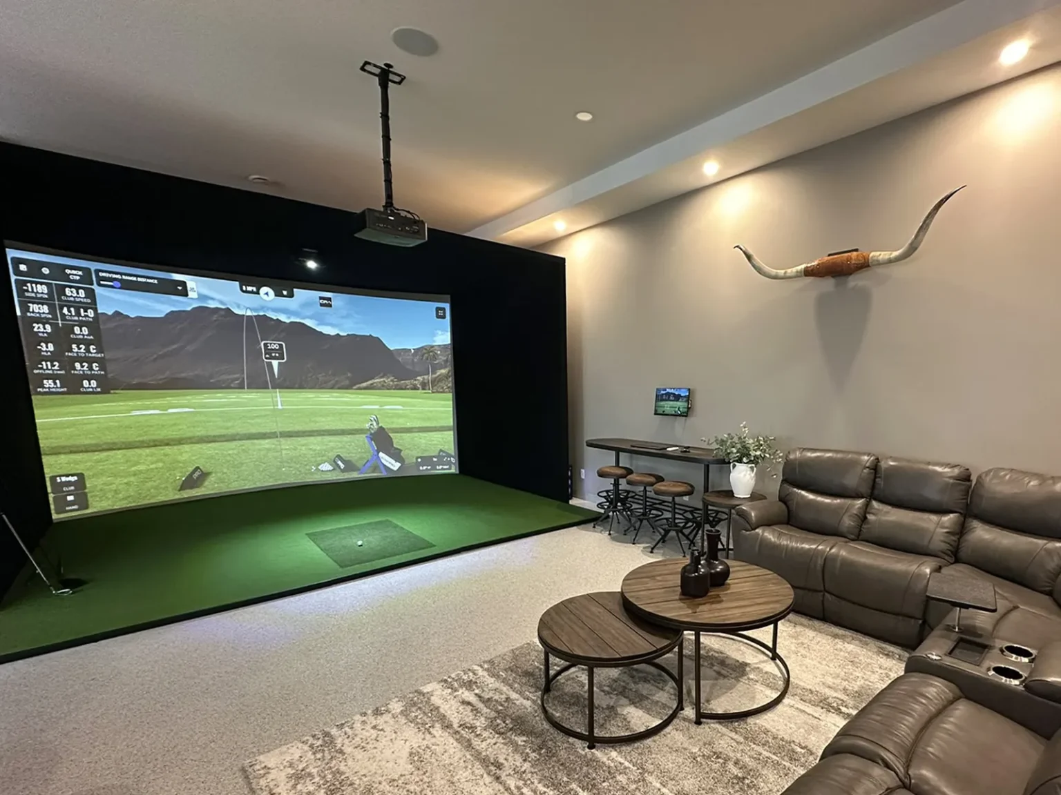 Golf simulator lounge with curved impact screen, turf, bar-height table and sectional seating