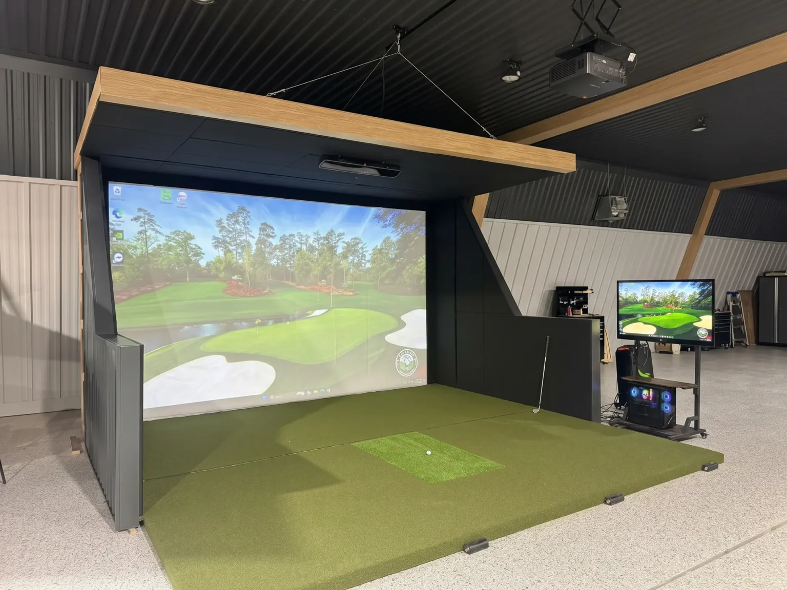 Custom framed golf simulator enclosure in a shop in Assiniboia, Saskatchewan, with turf, acoustic panels and an overhead projector